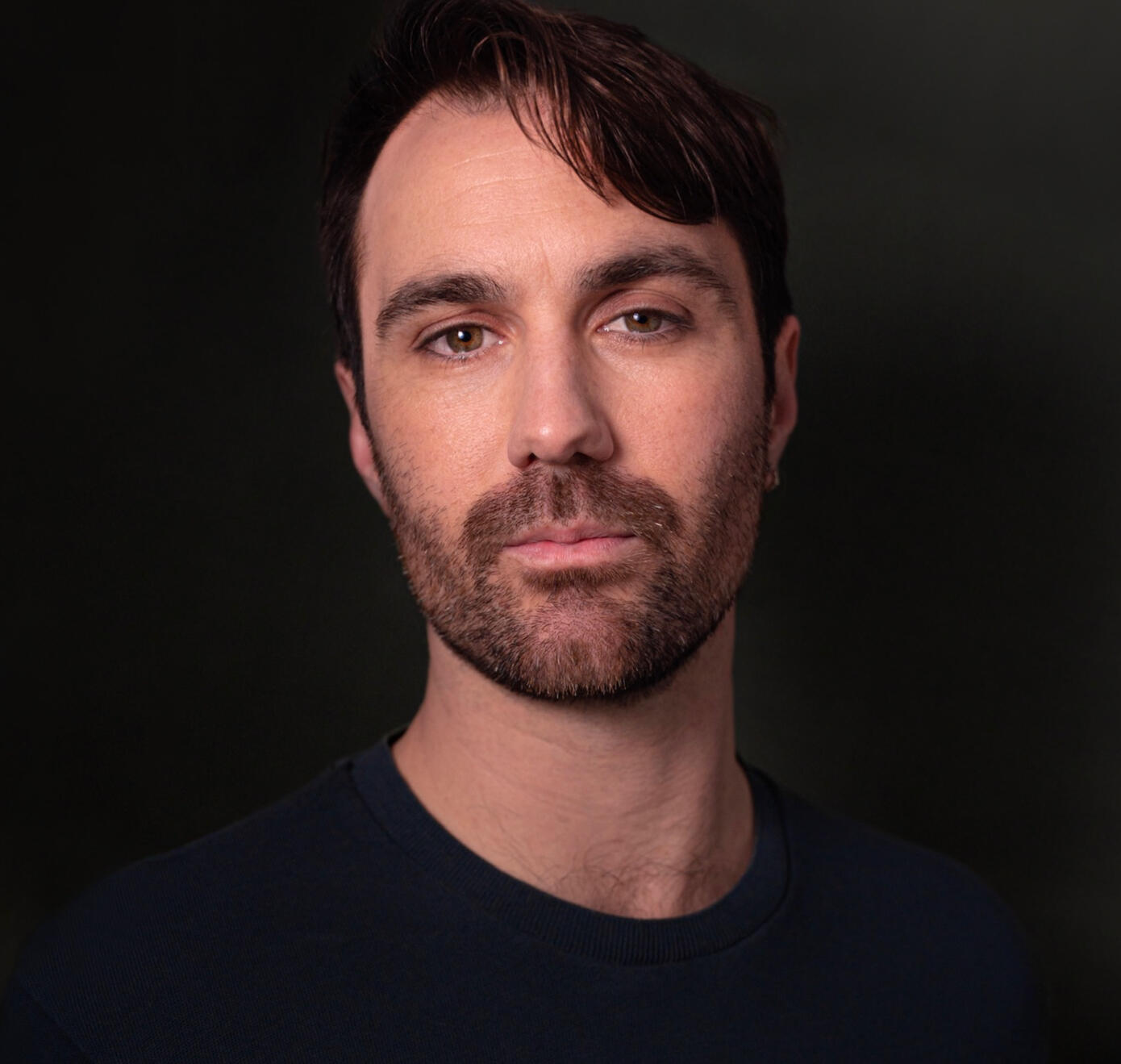 Headshot of Ryan Pater wearing a black shirt, with a black background
