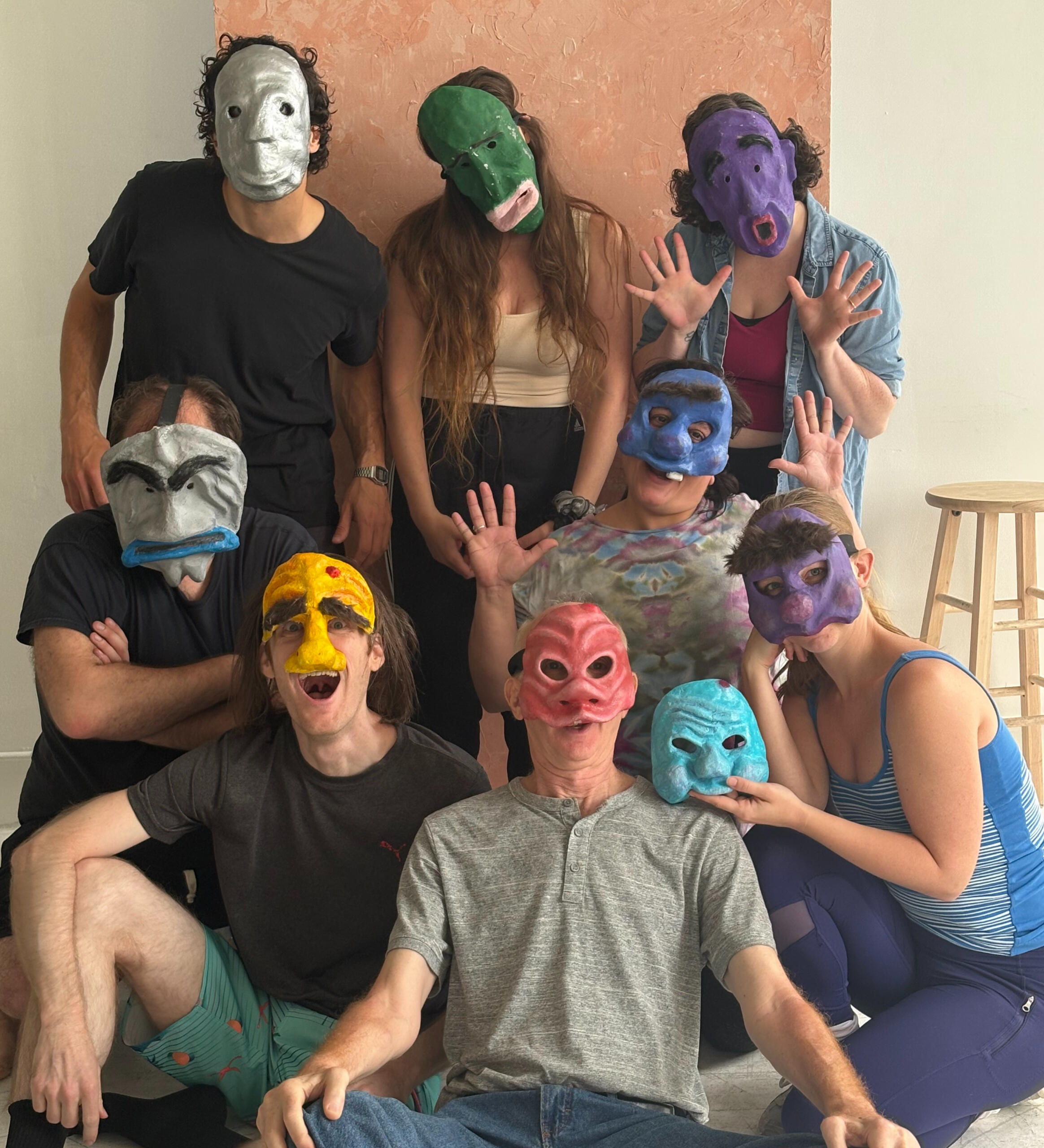 A group of people sitting, kneeling and standing wearing colorful masks